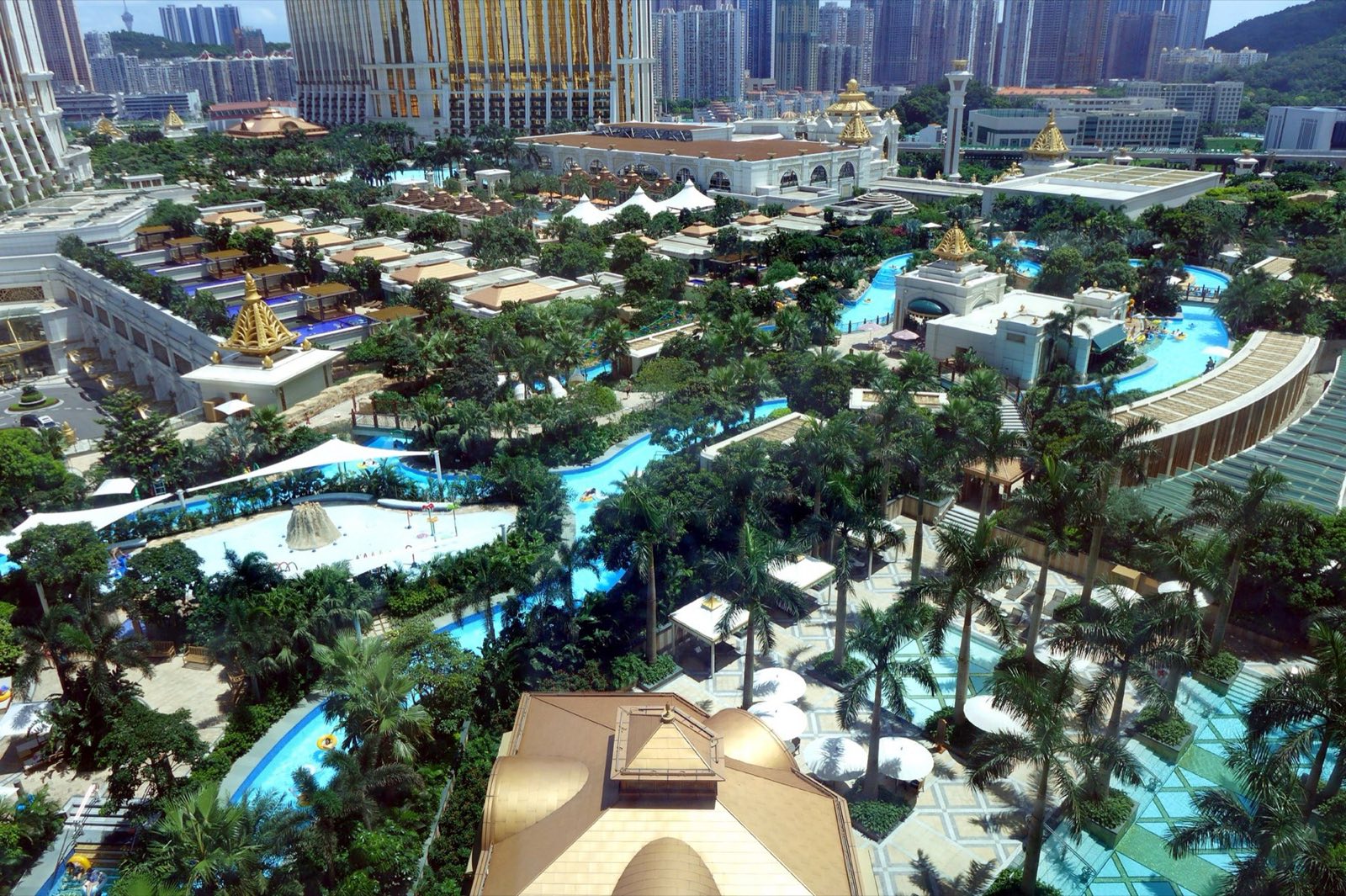 Aerial view of Galaxy Macau’s Grand Resort Deck, with palm-lined lazy rivers and pools beneath gold-crowned casino hotel towers