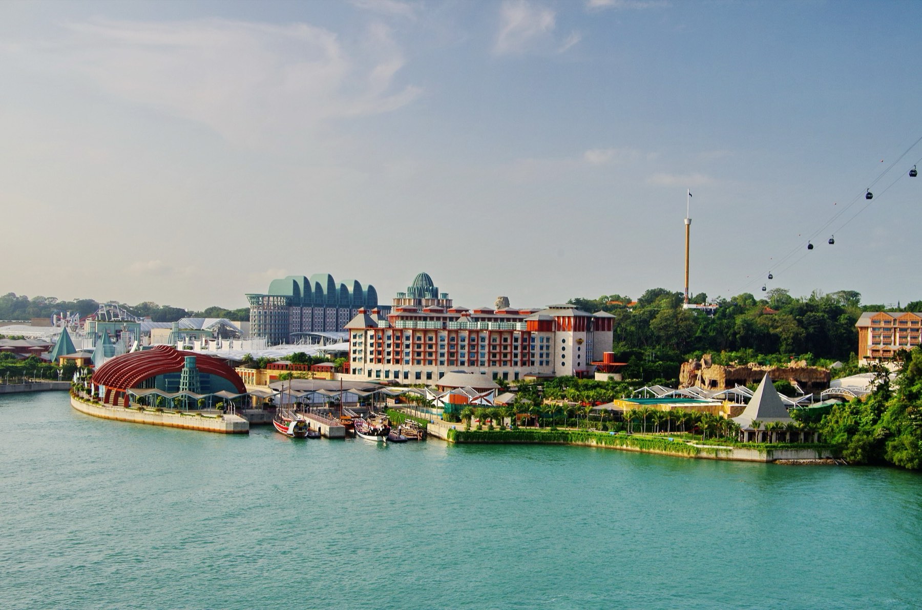 Resorts World Sentosa seen across turquoise water from the Singapore Cruise Centre, with hotel towers, a red-domed pavilion and the cable car line